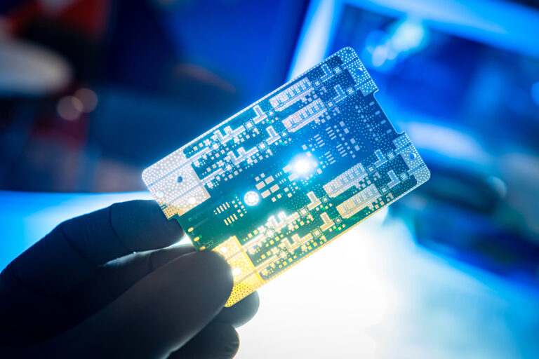 Computer board in hand of a man. Small printed circuit board close-up. Bright light shines through circuit board. Concept - repair or installation of PCB. Hand with PCB on a blurred background.